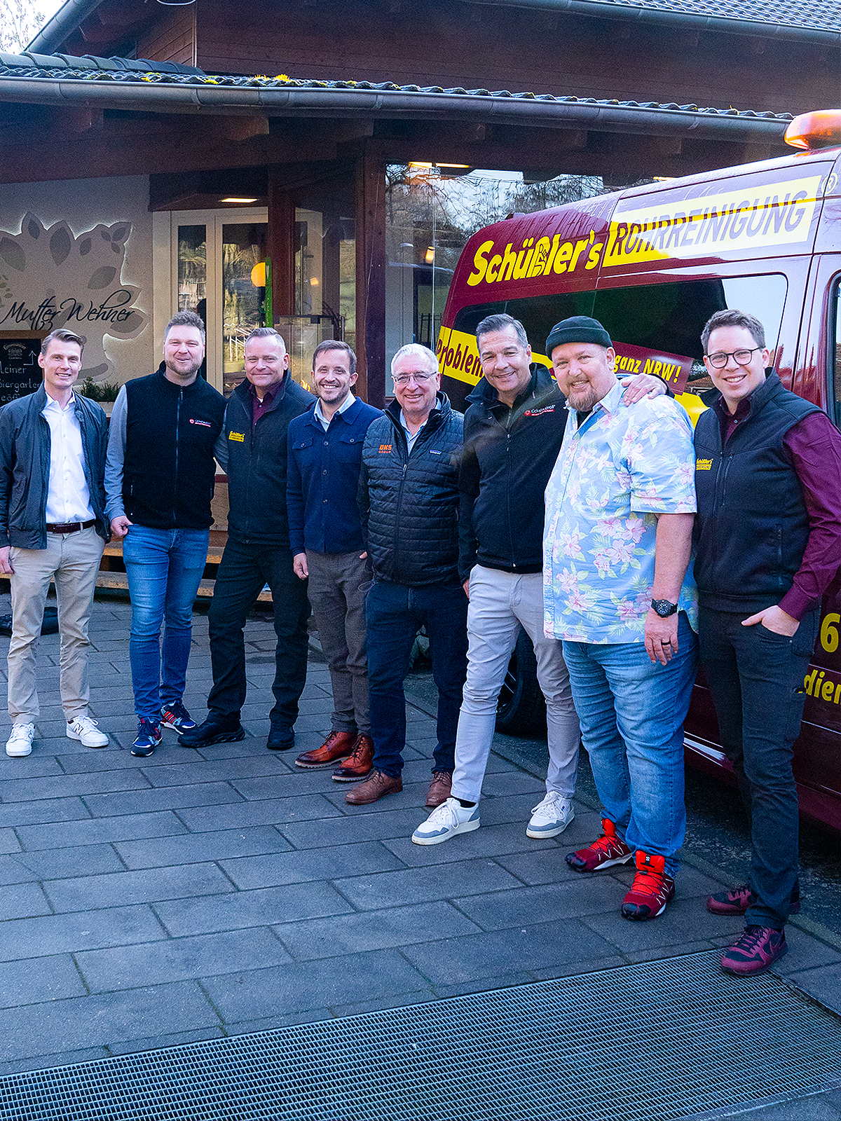 Eine Gruppe von Männern von der DKS Group und Schüßler's Rohrreinigungsschnelldienst stehen vor einem Auto